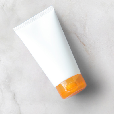 white tube of suncream with orange cap on neutral background